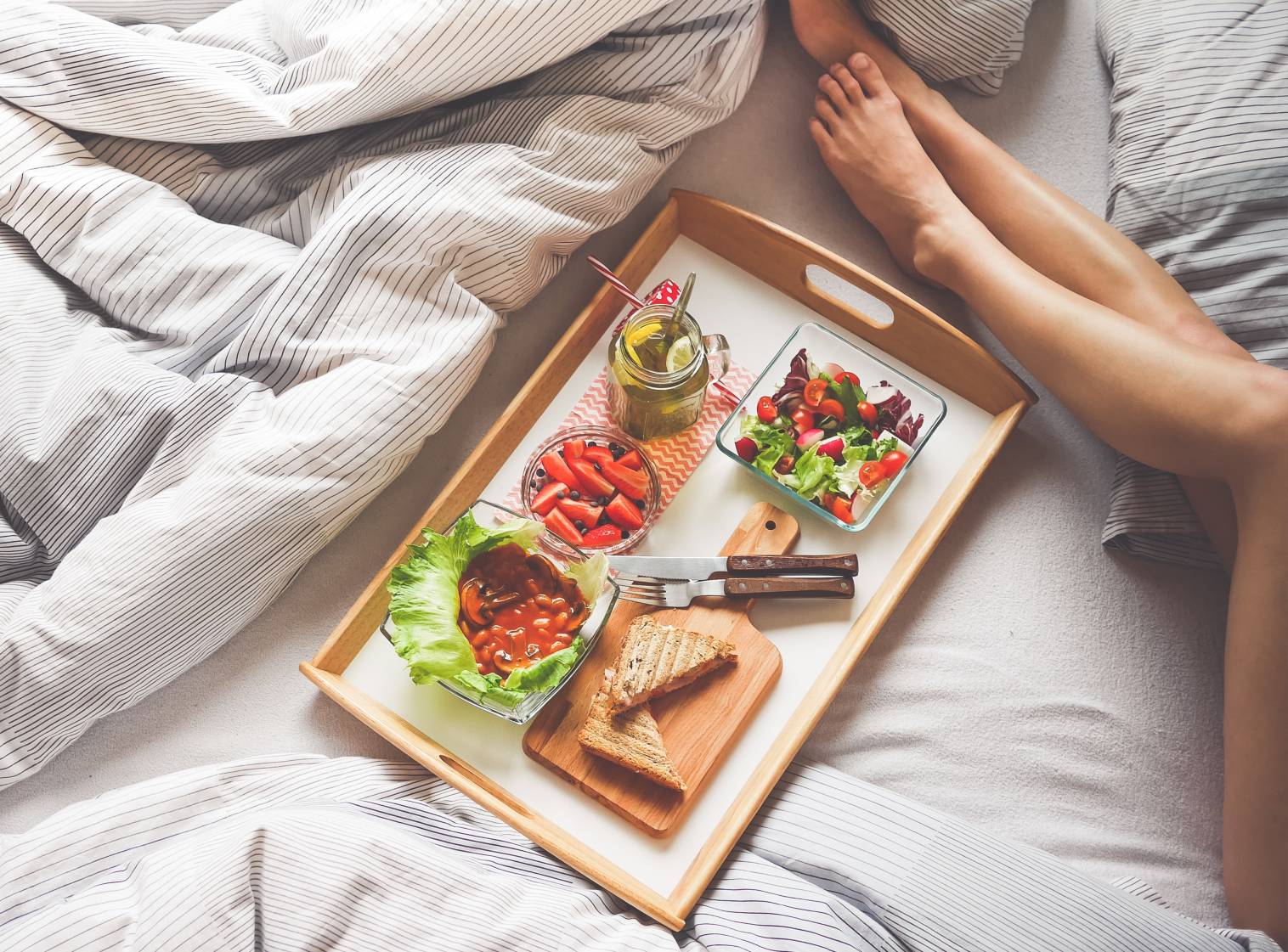 perna de mulher na cama com bandeja de comidas saudaveis